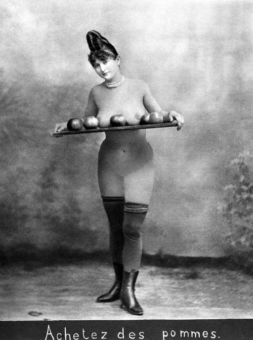a topless woman displays apples by her breasts on a board