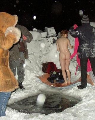 nude woman prepares to jump through a hole in the sea ice in the dark while it is snowing