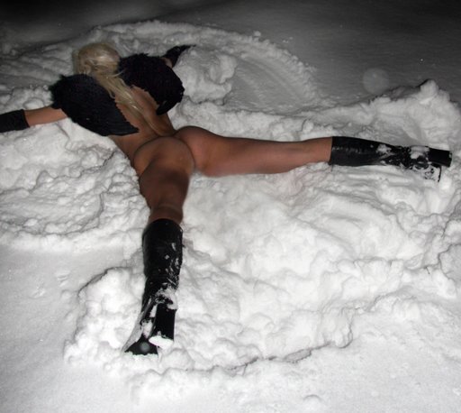 woman in black leather with dark feather wings face down in the snow making snow angels