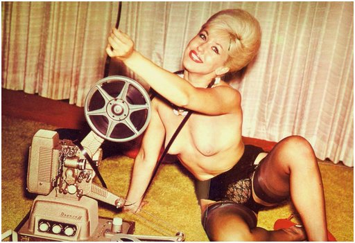 color photo of a blonde in fine lingerie threading an 8mm or 16mm movie through her projector