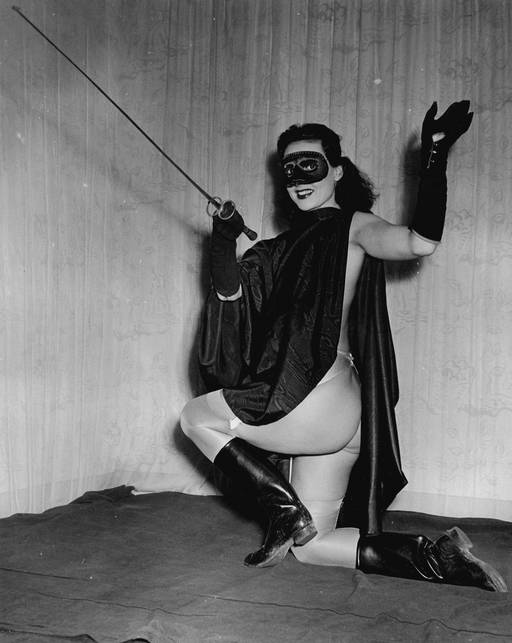 burlesque dancer in highwayman costume with mask and cape and sword and boots (and no pants)