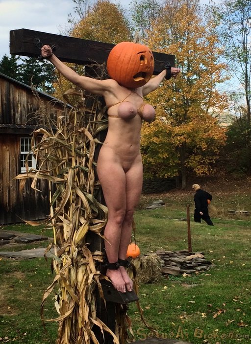 crucifixion of a bondage model with a pumpkin on her head posed as a scarecrow