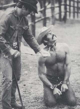 gay cowboy in bondage cuffs wearing a collar and a leash