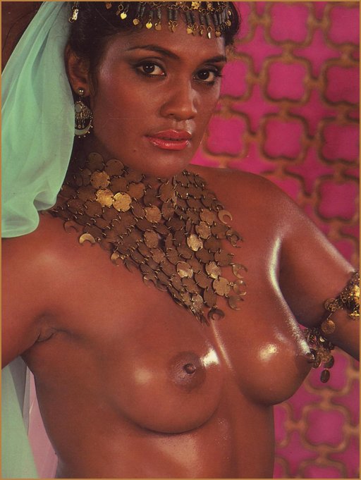 black woman with bare breasts, oiled skin, coin belt, and white scarf or veil