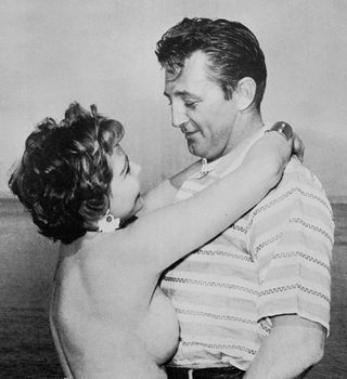 actor Robert Mitchum getting a hug from a topless woman
