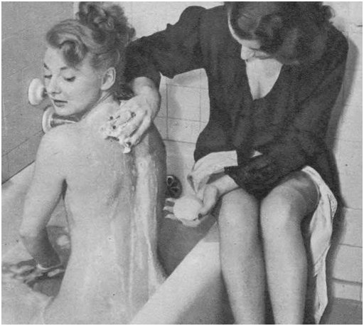 well dressed woman sits on edge of tub and helps pretty girl scrub her back in the bathtub