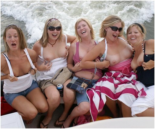 five happy looking women on the back of a power boat smiling and laughing and baring their tits for the camera
