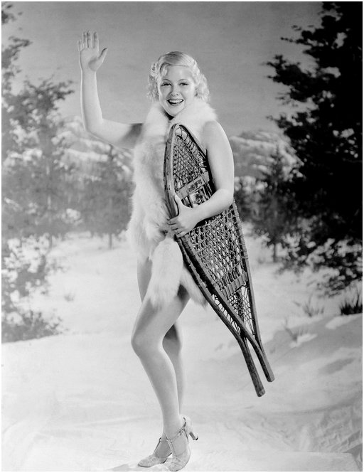 nude looking actress Mary Carlisle wrapped in nothing but a few strands of fur standing in the snow with a pair of snow shoes under her arm