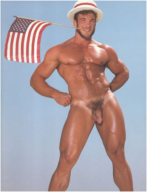 naked very buff gay man grinning with an American flag clenched between his teeth