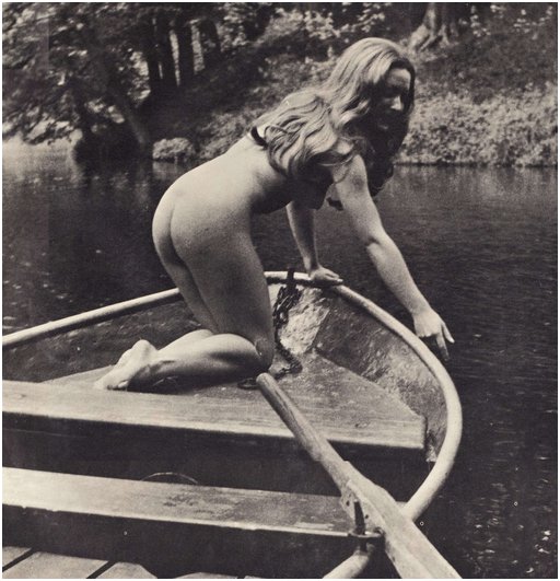 naked woman kneeling in the bow of a rowboat, trailing one hand in the water of a river or perhaps a bayou