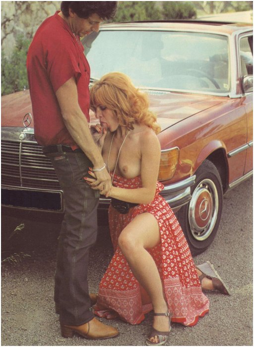 woman in a dress with her tits out kneeling beside a 1970s car to give the driver a blowjob