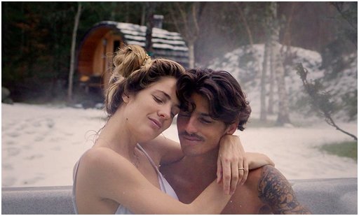 bikini woman and shirtless man lounge in a hot springs near a cozy cabin in winter